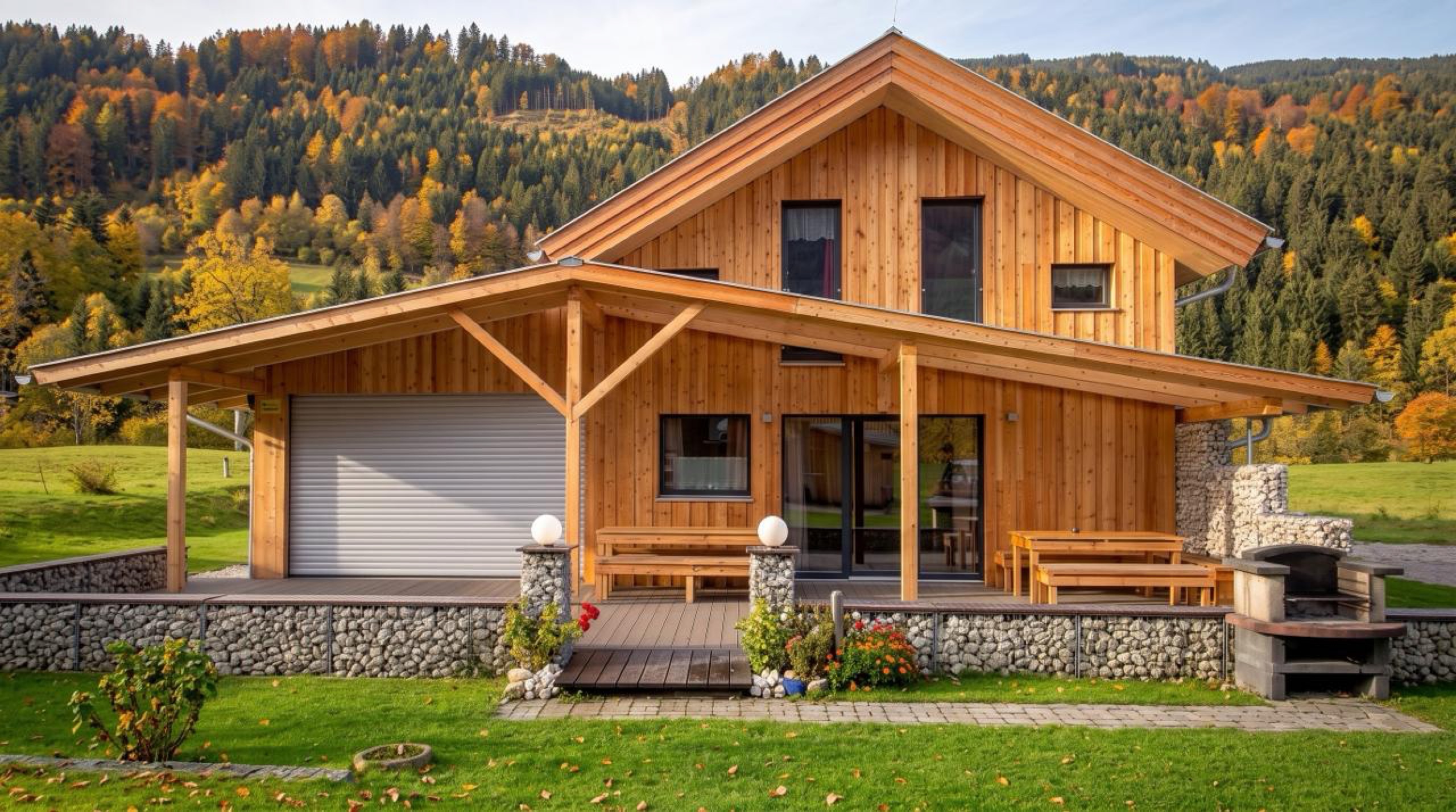 Frontansicht des Wellness-Chalets mit Holzterrasse und Garten im Herbst